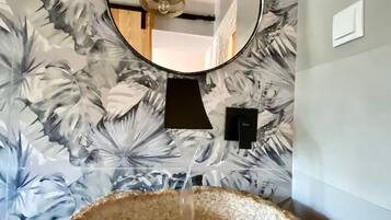 A bathroom with a stone sink, a mirror, and a floral wallpaper.
