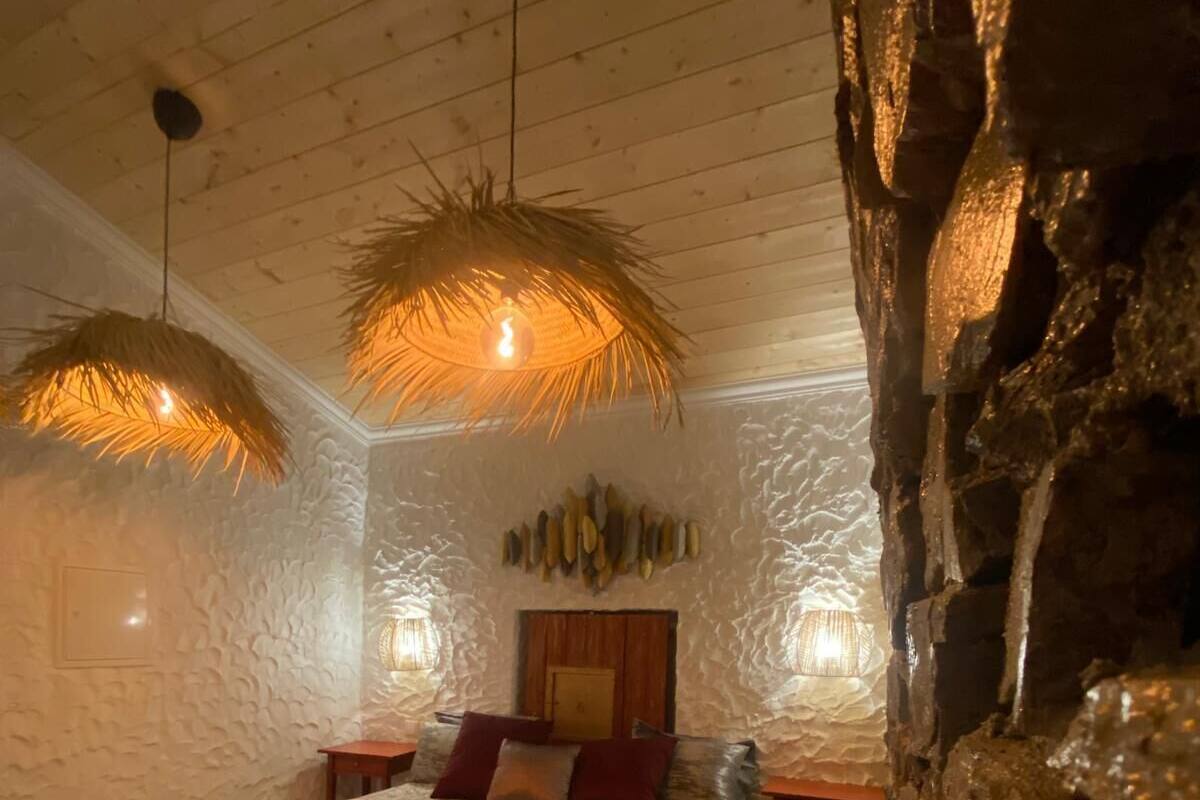 A bedroom with a large bed, two nightstands, a stone wall, and a ceiling with wooden beams.