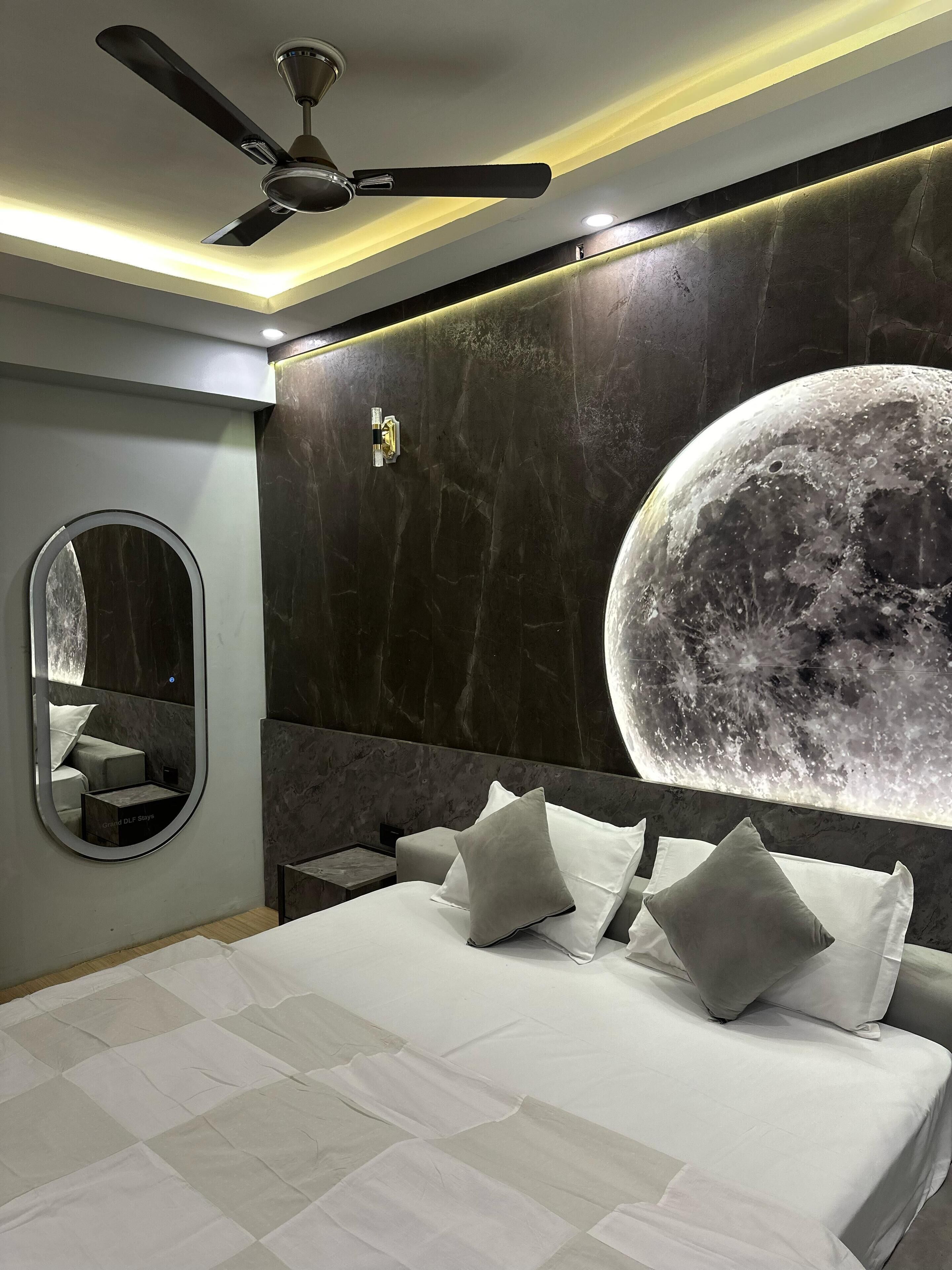 A bedroom with a large bed, a ceiling fan, a wall-mounted mirror, and a large moon mural.