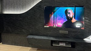 A modern interior with a curved wall-mounted TV displaying a person. - Villa Vistosa Gomti Nagar (Lucknow)