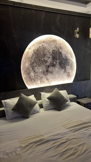 Une chambre à coucher avec un grand lit, de nombreux oreillers et un luminaire mural en forme de lune.