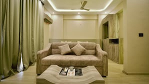 A modern living room with a beige sofa, a coffee table with magazines, and a ceiling fan. - Villa Vistosa Gomti Nagar (Lucknow)
