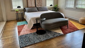 Un dormitorio con cama, un sillón gris, una mesita auxiliar y una planta en maceta.