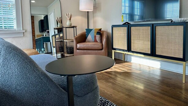 Una sala de estar moderna con un sofá, una mesa redonda, una silla, un mueble con paneles trenzados y un televisor.