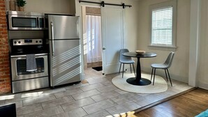 Una cocina moderna con electrodomésticos de acero inoxidable, un comedor con una mesa redonda y dos sillas, y una ventana con persianas.