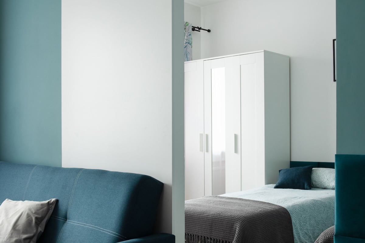 A modern room with a blue sofa, a bed with a blue headboard, and a white wardrobe.