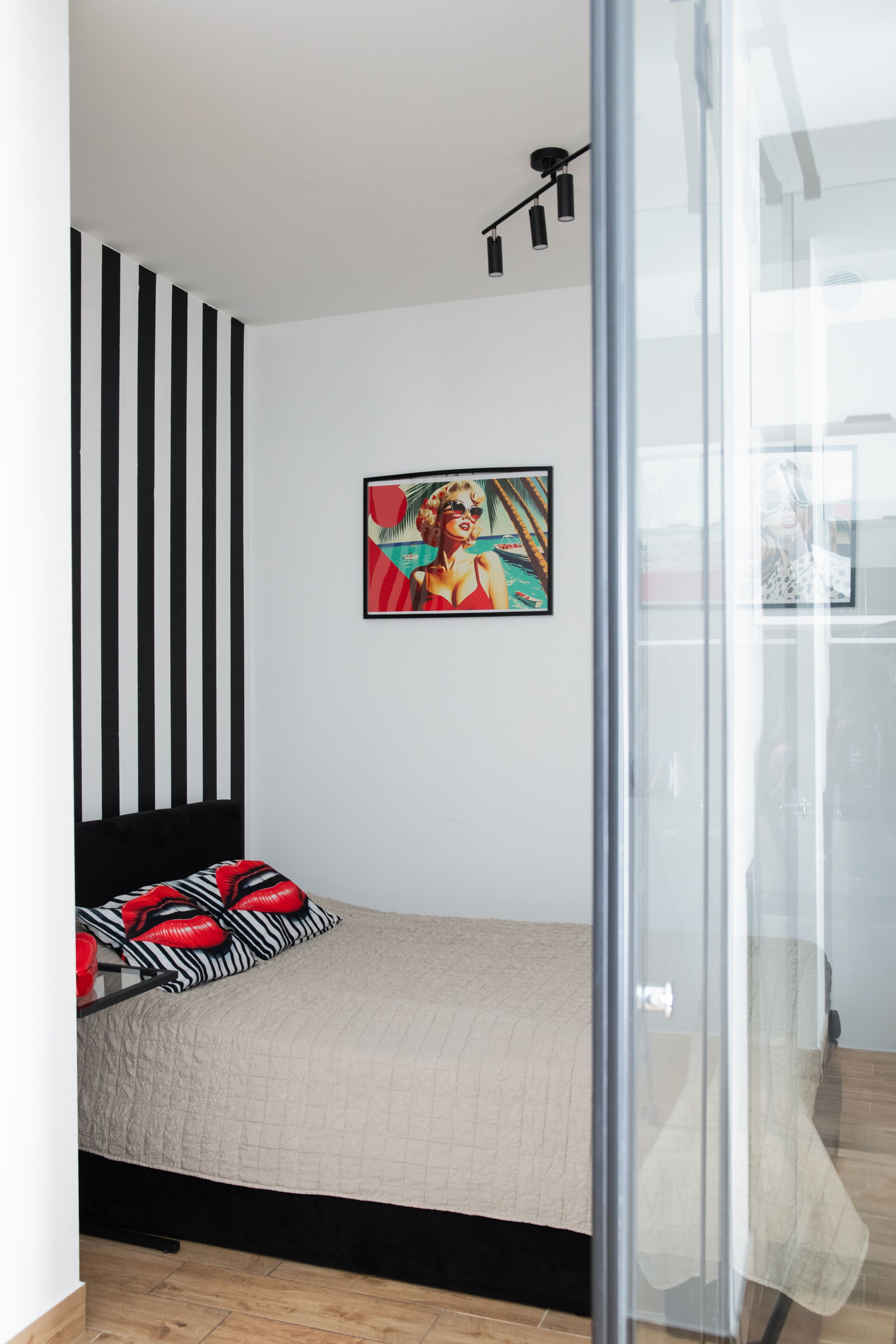 Un dormitorio con cama, pared a rayas blanco y negro, un cuadro y una puerta de cristal.