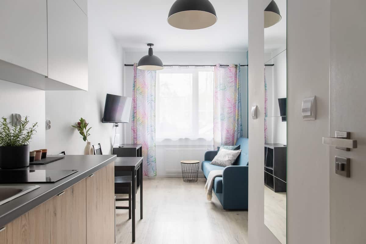 A modern kitchen with a wooden countertop, a dining area with a table and chairs, a blue sofa, and a large window with colorful curtains.
