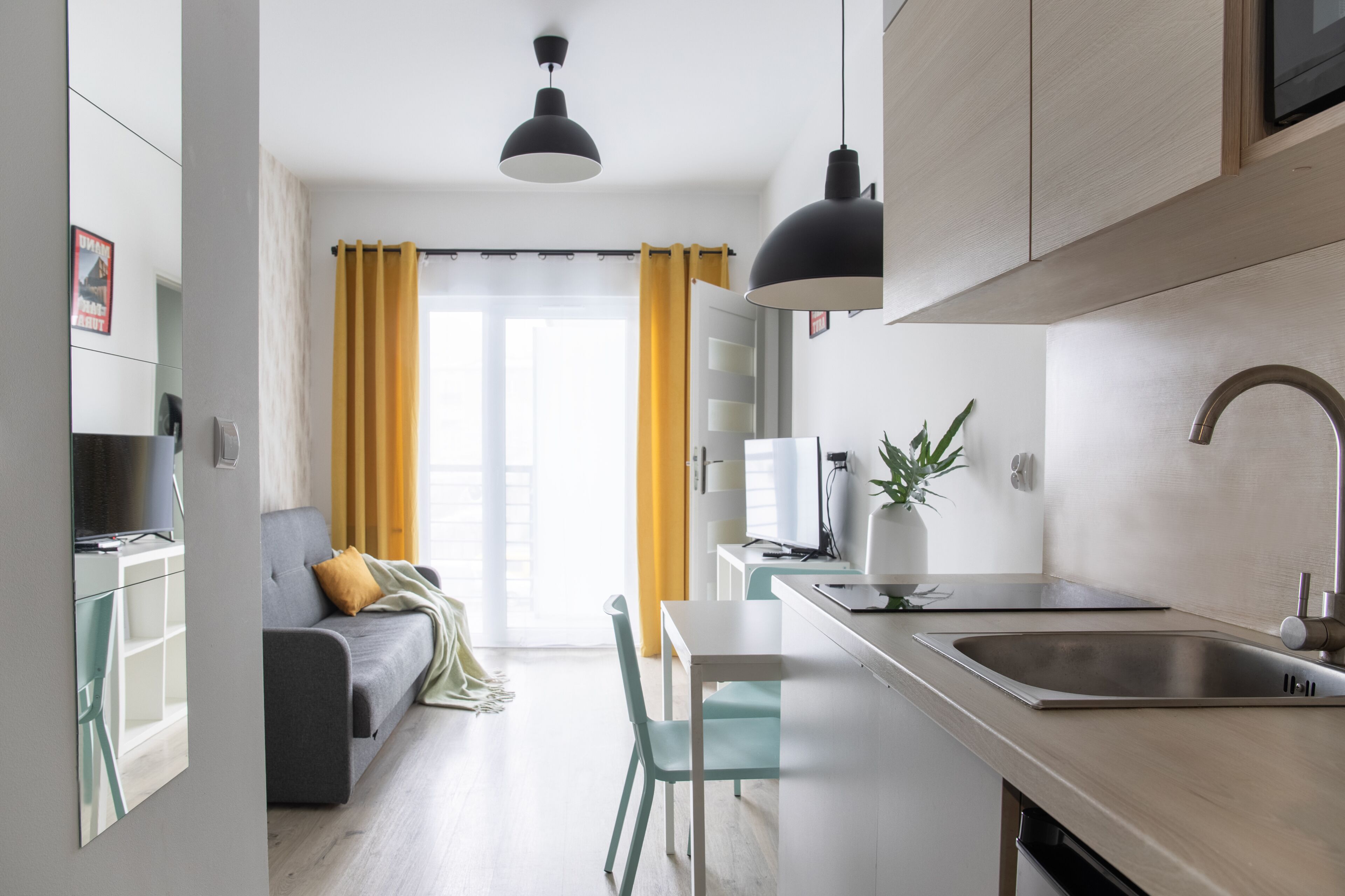 A modern kitchen with a sink, a dining area with a table and chairs, a sofa, and a television.