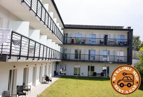 Un edificio moderno a più piani con balconi, area salotto esterna e un logo che indica un servizio di autonoleggio.