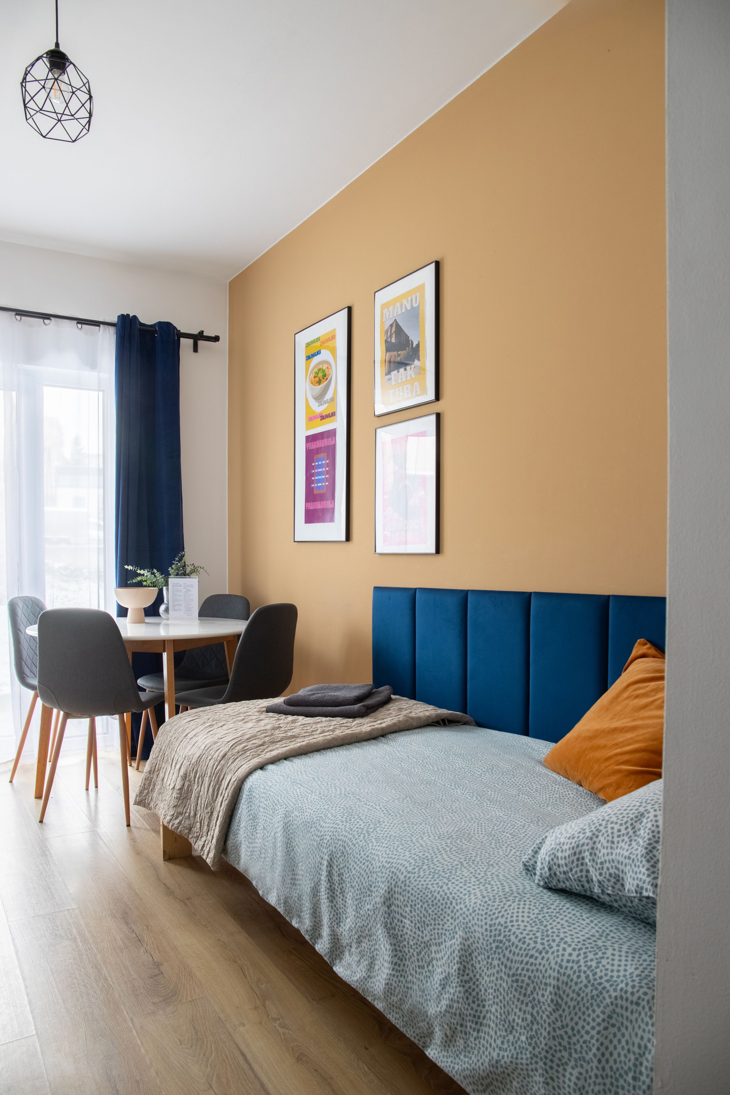 A modern hotel room with a bed, a desk, chairs, and a window with curtains.