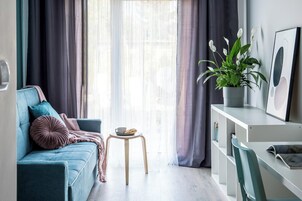 Una sala de estar moderna con un sofá azul, un taburete de madera, una planta en maceta y una consola blanca con un cuadro enmarcado.