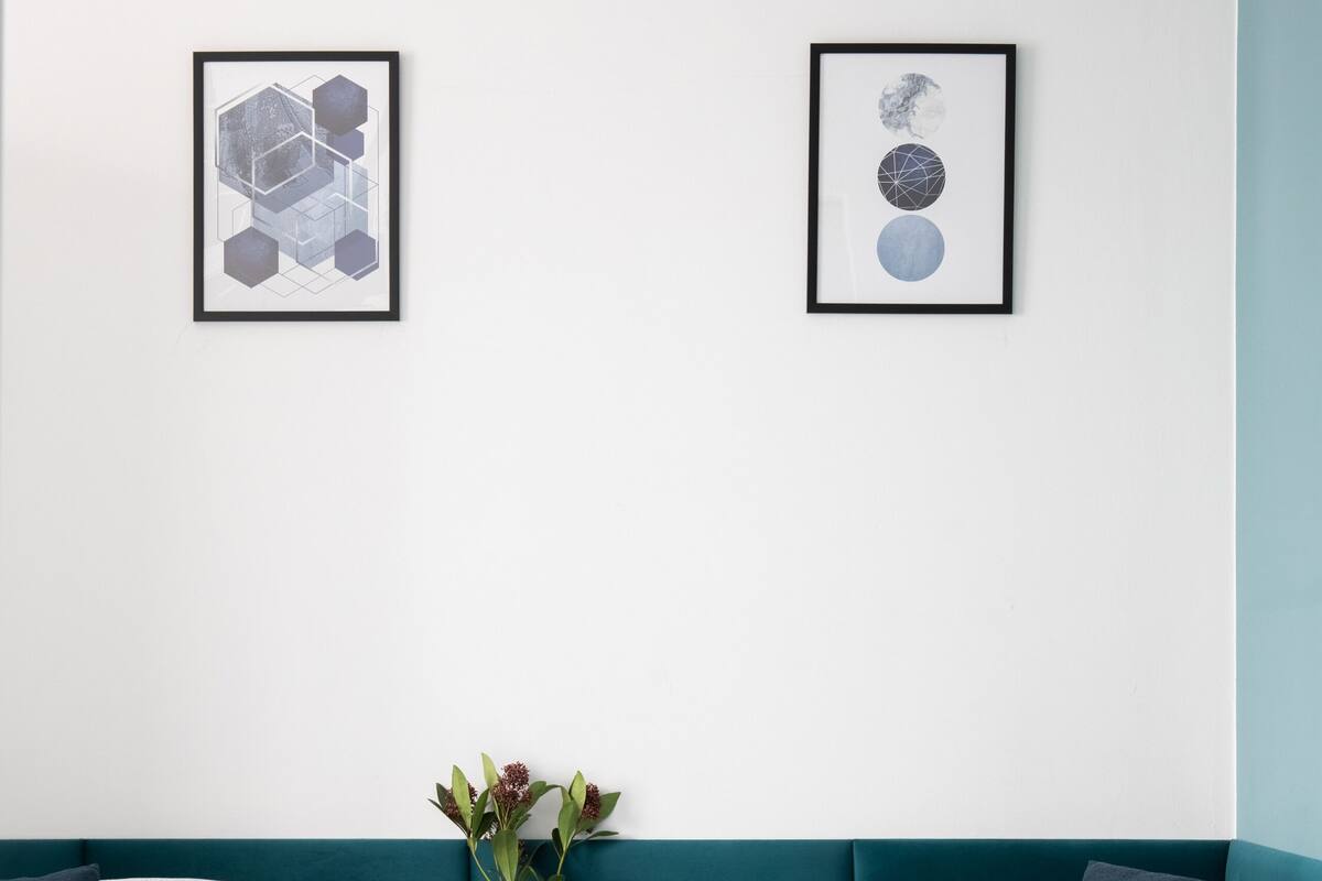 A bedroom with two beds, a nightstand with a vase, and two framed artworks on the wall.