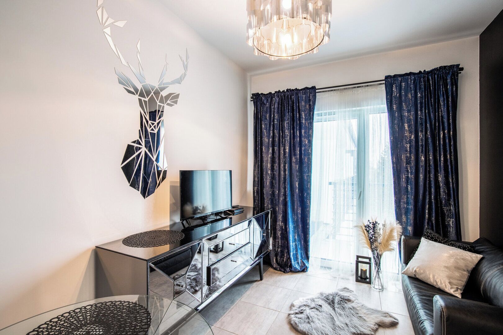 A modern living room with a glass coffee table, a flat-screen TV, a leather sofa, and a decorative wall piece.
