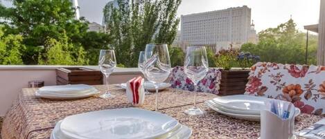 A table set outdoors with plates, glasses, and cutlery, overlooking a cityscape with buildings and trees.