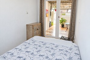 A bedroom with a bed, a wooden cabinet, and a view of an outdoor patio with a table and chairs.