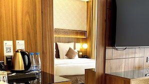 A hotel room with a bed, bedside table with a kettle, water bottles, and a TV.
