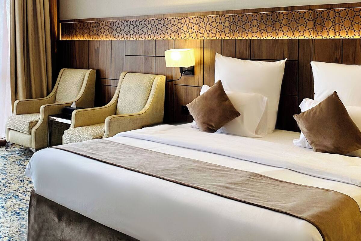 Een hotelkamer met een groot bed, twee fauteuils, een nachtkastje en een wandlamp.