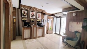 A modern hotel lobby with a reception desk, framed pictures, and a seating area with a chair.