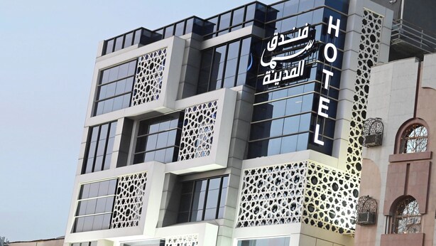 A hotel building with a modern architectural design, featuring multiple balconies and decorative lattice patterns on the facade.