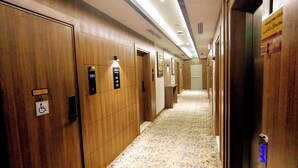 A hotel hallway with wooden walls, numbered doors, and a carpeted floor.