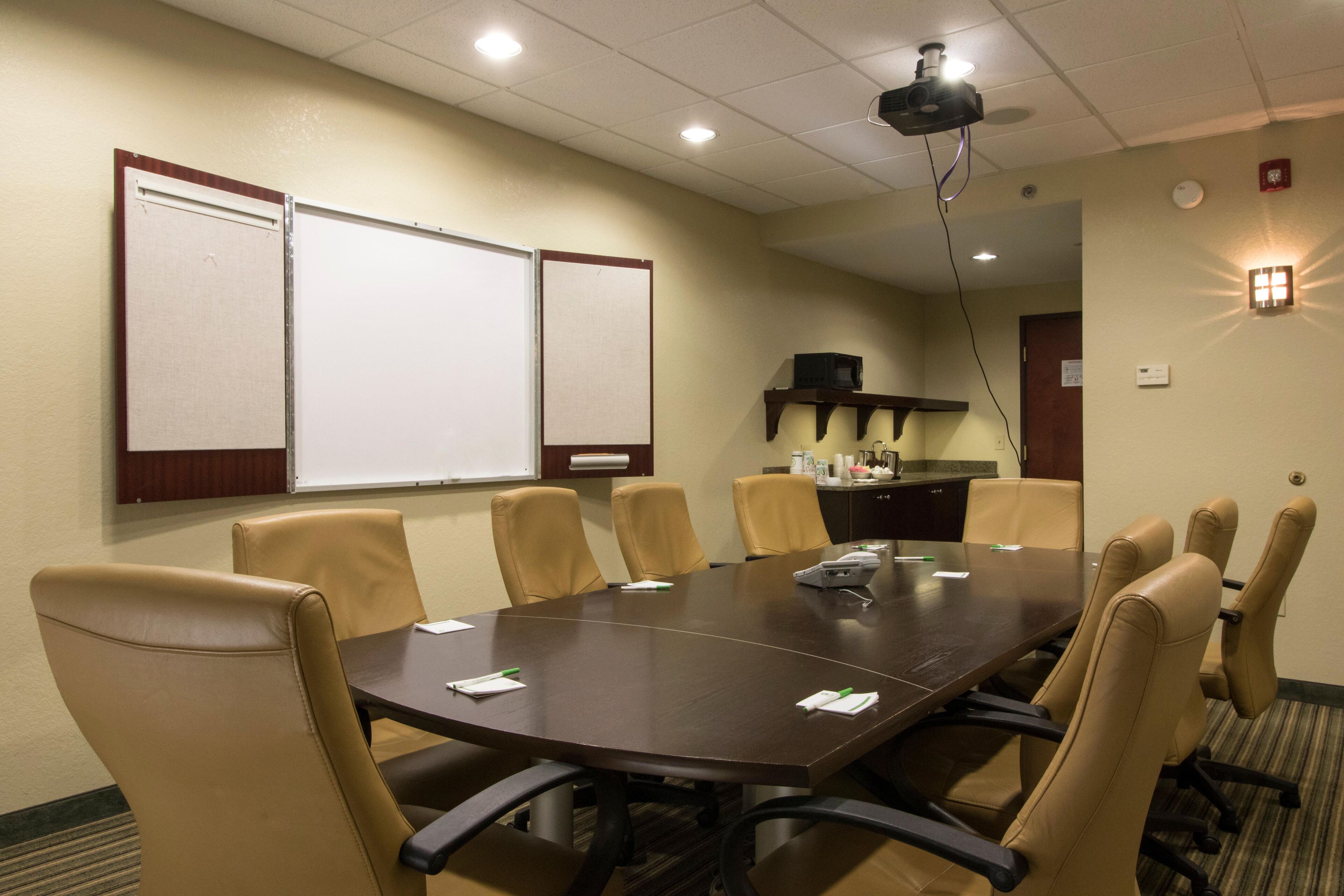 A conference room with a large table, six chairs, a projector, whiteboards, and a small kitchenette area.