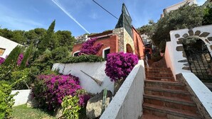 A residential building with a stone staircase, a white wall with a stone archway, and purple bougainvillea flowers. - Exceptional villa with panoramic sea views AV 81 (ROSES)
