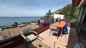 A terrace with a table and chairs, a view of the sea, and a building with a tiled roof. - Exceptional villa with panoramic sea views AV 81 (ROSES)