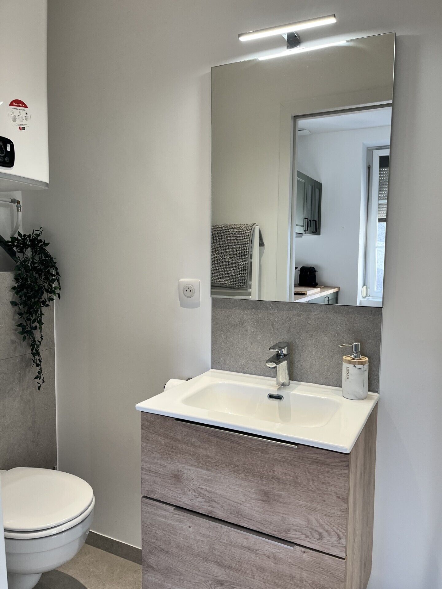 A modern bathroom with a white sink, wooden cabinet, and a large mirror.