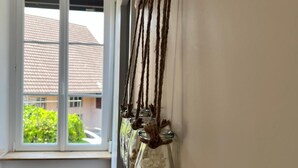 Un couloir avec une fenêtre, un plancher en bois et une décoration murale composée de bouteilles en verre transparent contenant des fleurs séchées.