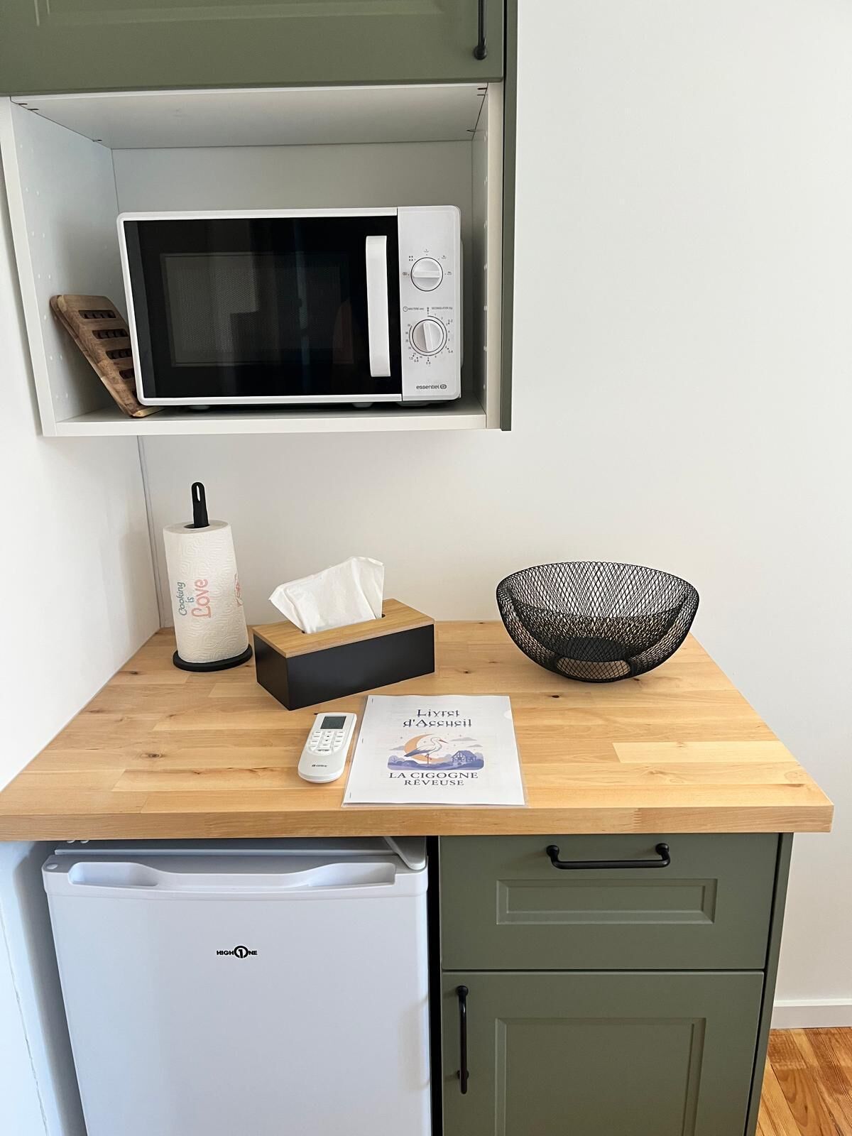 A kitchen with a microwave, a small refrigerator, a wooden countertop, a tissue box, a bowl, and a menu.