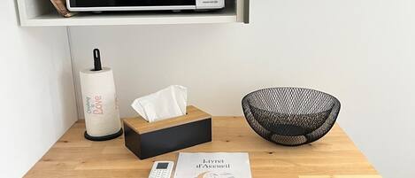 A kitchen with a microwave, a small refrigerator, a wooden countertop, a tissue box, a bowl, and a menu.