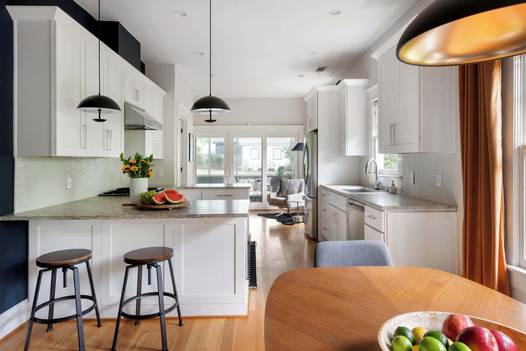 A modern kitchen with white cabinets, a large island with stools, and a view to the backyard.
