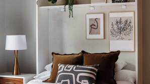 A bedroom with a bed, two pillows, a bedside table with a lamp, and two framed artworks on the wall.