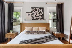 A bedroom with a large bed, two bedside tables, a headboard, and a window with curtains.
