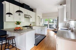 A modern kitchen with white cabinetry, a central island, a stove, and pendant lights.