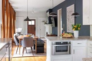 A modern kitchen with white cabinets, a central island with an oven, and a dining area with a round table and chairs. - Canvas Haven (Atlanta)