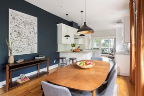A modern kitchen with white cabinets, a central island with a fruit bowl, pendant lighting, and a large abstract painting on the wall. - Canvas Haven (Atlanta)