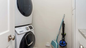A laundry room with a front-loading washer and dryer, a blue mop, and a vacuum cleaner.