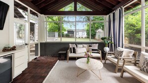 A cozy room with a large window, a wooden ceiling, and a view of a house and trees.