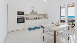 A modern kitchen with white cabinets, a built-in oven, and a dining area with a table and chairs.