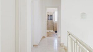 A hallway with white walls and a tiled floor leading to a bathroom with a shower and a toilet.