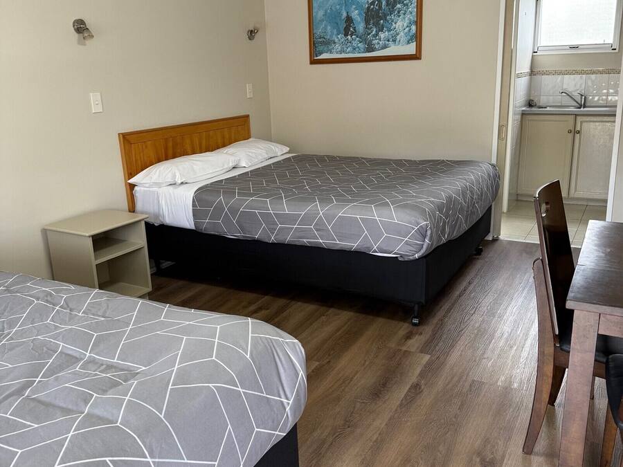 Habitación de hotel con dos camas, una mesita, una silla, un cuadro y una kitchenette.
