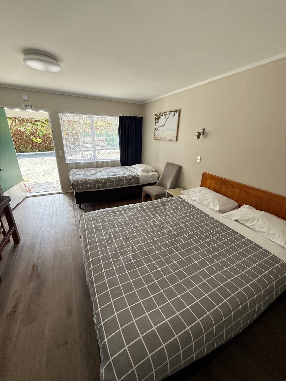 A room with a large bed, a smaller bed, a chair, and a desk. There is a window with curtains and a painting on the wall.