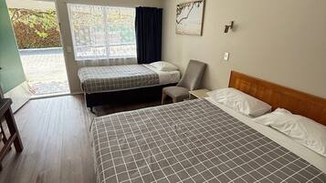 A room with a large bed, a smaller bed, a chair, and a desk. There is a window with curtains and a painting on the wall.