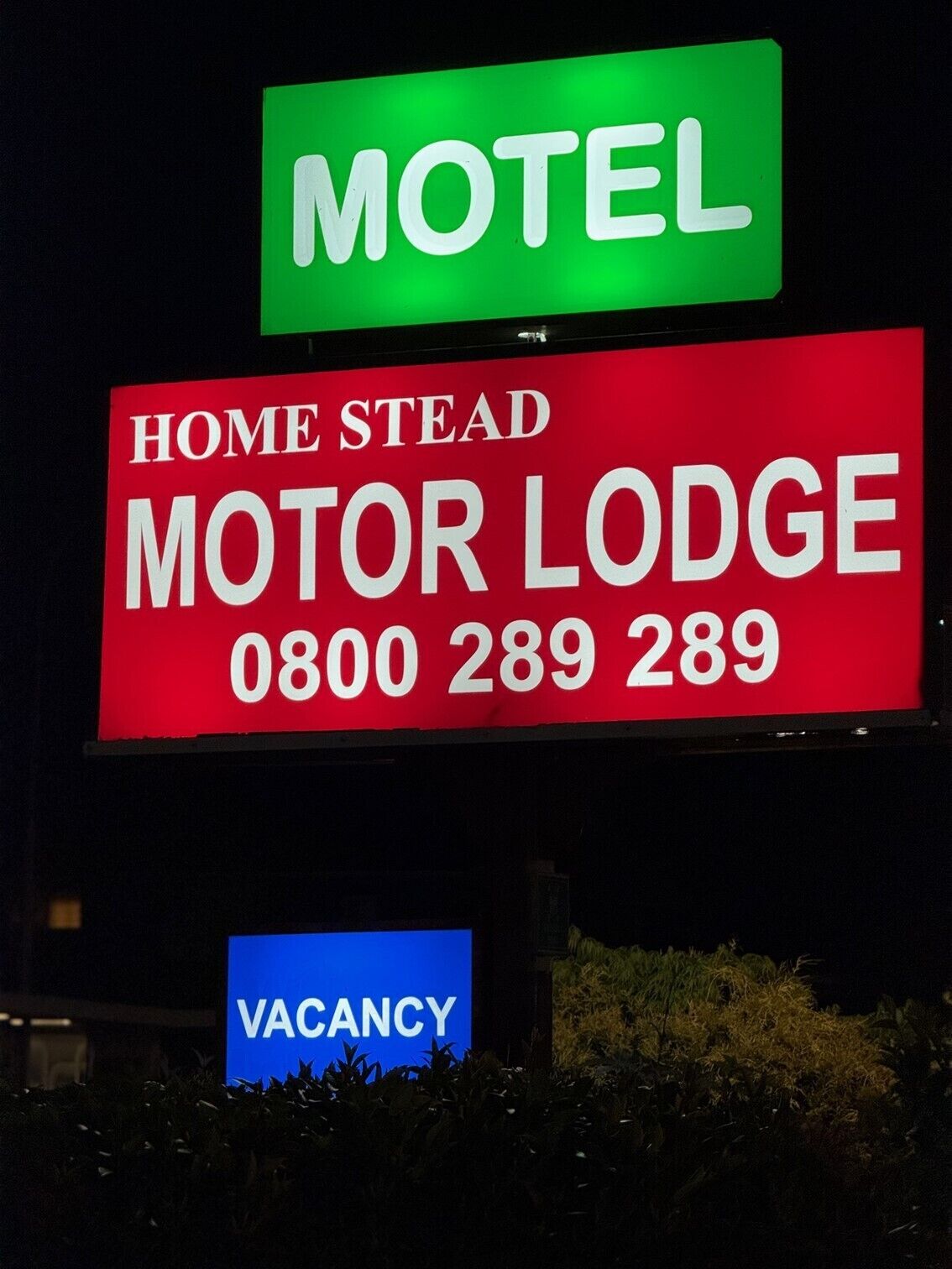 Een motelbord met 'MOTEL' in het groen, 'HOME STEAD MOTOR LODGE' in het rood, en een 'VACANCY'-bord eronder.