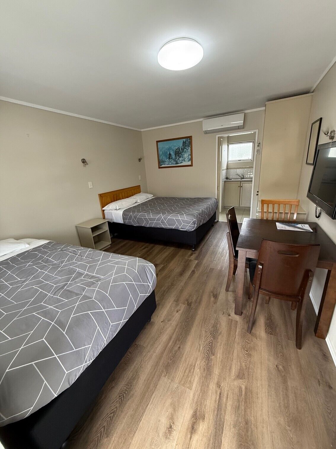 A hotel room with two beds, a desk, a chair, a TV, and a painting on the wall.