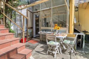 A patio with a table and chairs, a staircase, and a window with sunflowers.