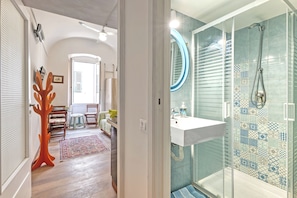 A bathroom with a glass shower enclosure, a white sink, and a patterned tile wall.
