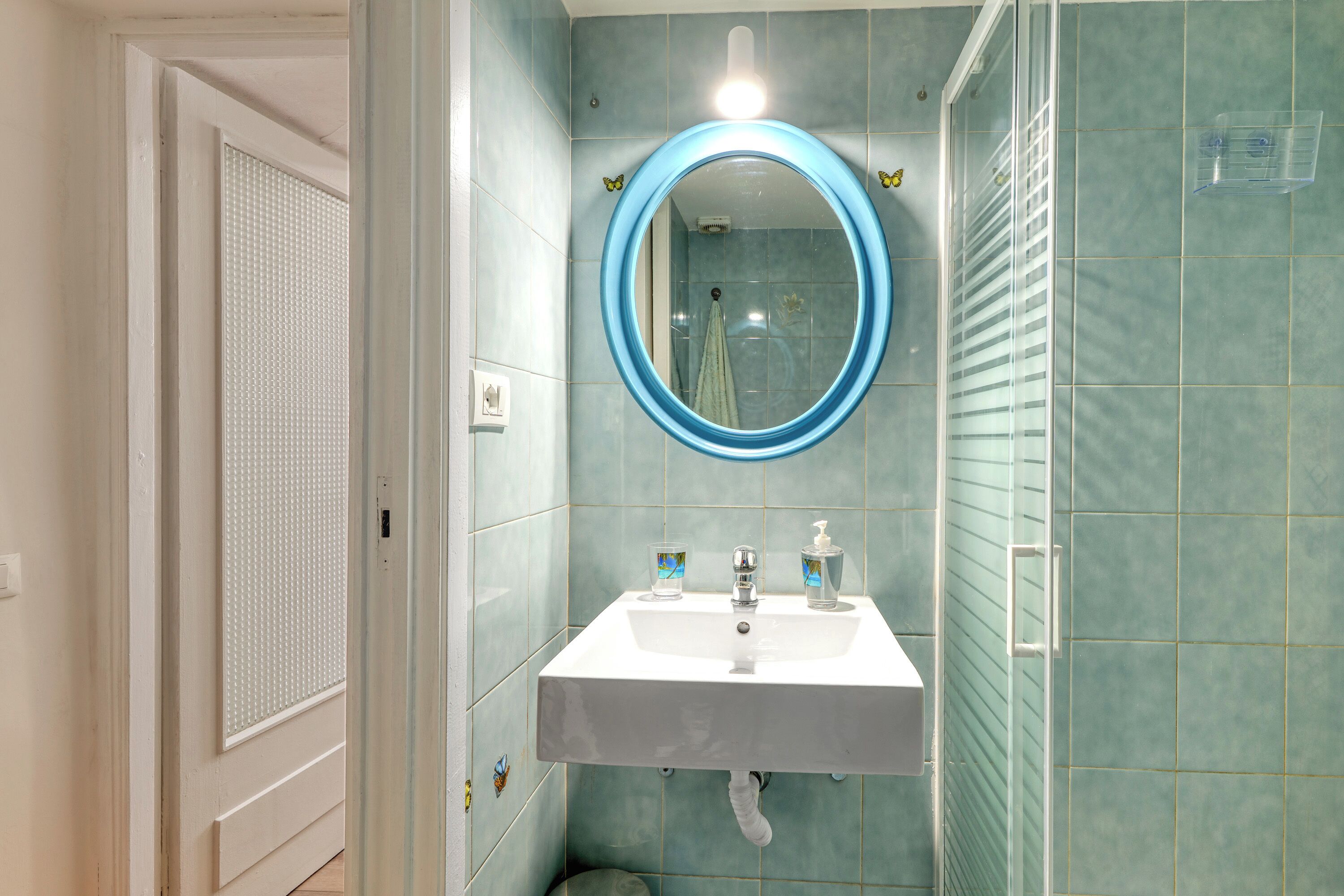 Un bagno con un lavandino bianco, uno specchio con cornice blu e una doccia con porta in vetro.